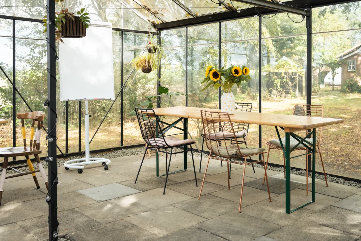 Lichte kas met tafels, stoelen en whiteboard voor een workshop in Breda