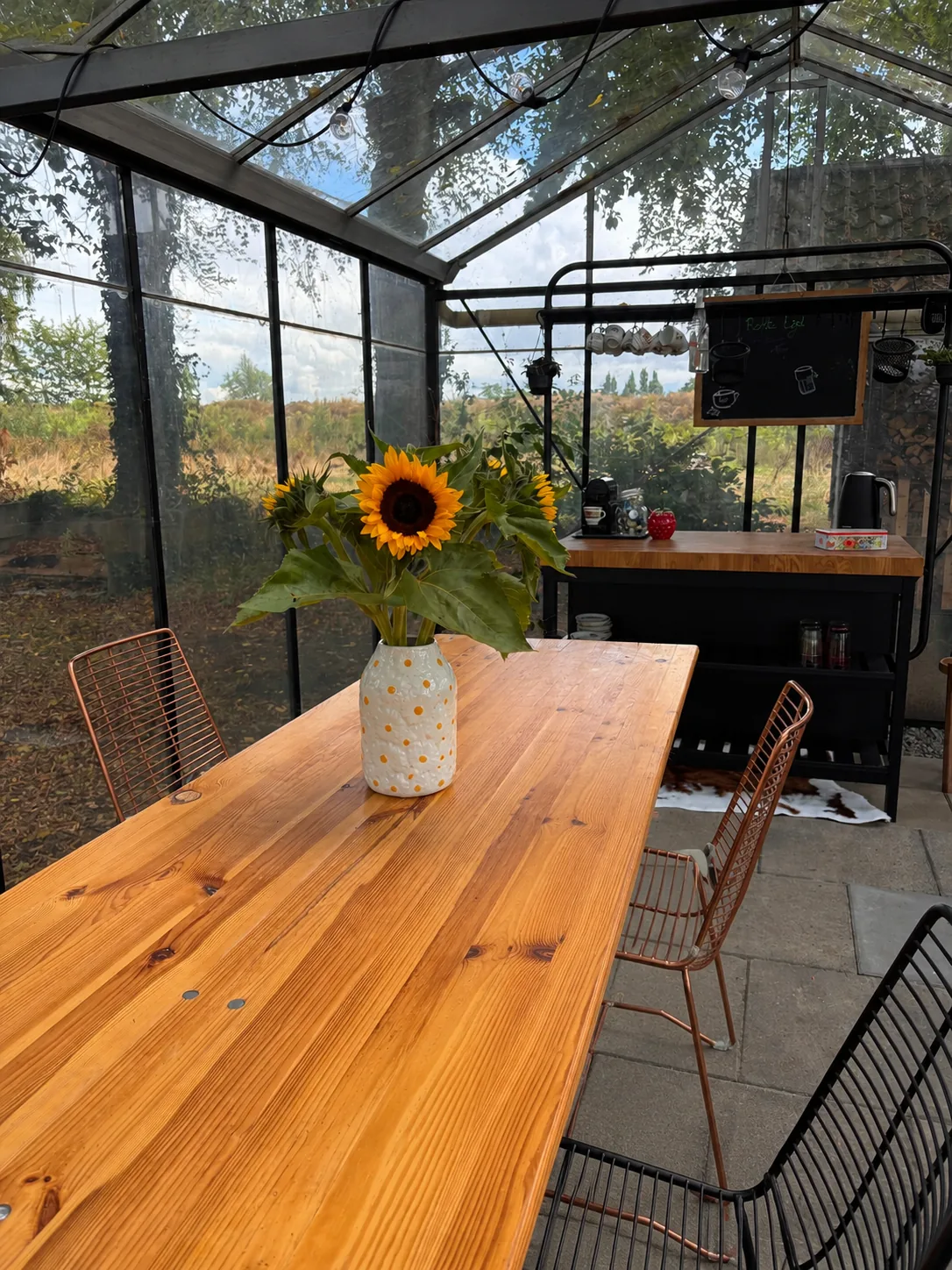 De verwarmde kas van Boerderij Ons Buiten met lange houten tafel, stoelen, keukeneiland en uitzicht op het groen